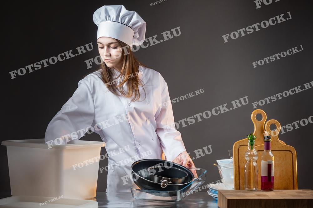 Молодая женщина-повар в белой униформе убирает кухонные принадлежности на опустевшей кухне, символизируя закрытие ресторана из-за банкротства. Пустая обстановка и собранные кухонные принадлежности создают атмосферу завершения работы заведения и его финансовых трудностей.
